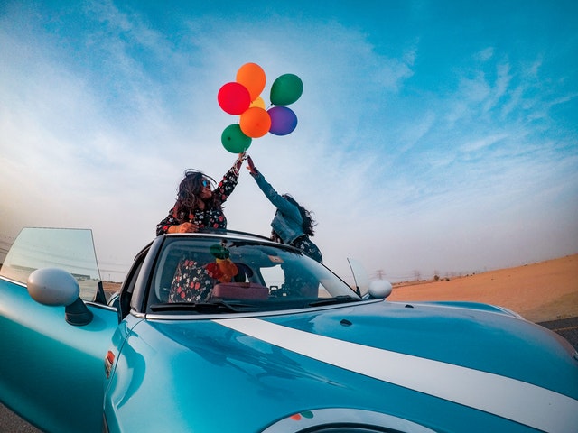 Ženy sedia v modrom aute a v rukách držia zväzok farebných balónov.jpg