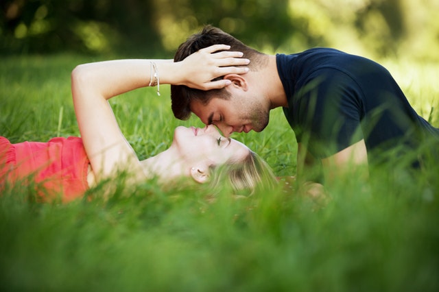 Muž a žena ležia v tráve a bozkávajú sa 
